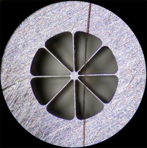 Увеличенная фотография предыдущей детали, сделанная через объектив микроскопа. Для сравнения сверху перемычек лежит человеческий волос. Секторы вырезаны на станке АРТА 122 НАНО